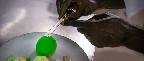 A person preparing a dish with a green spherical item on a plate, surrounded by green and white elements.