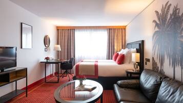 Una habitación de hotel con cama, televisión, escritorio, sofá y mesa de centro.