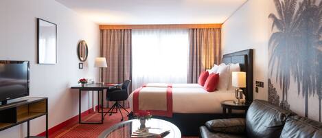 A hotel room with a bed, a TV, a desk, a sofa, and a coffee table.