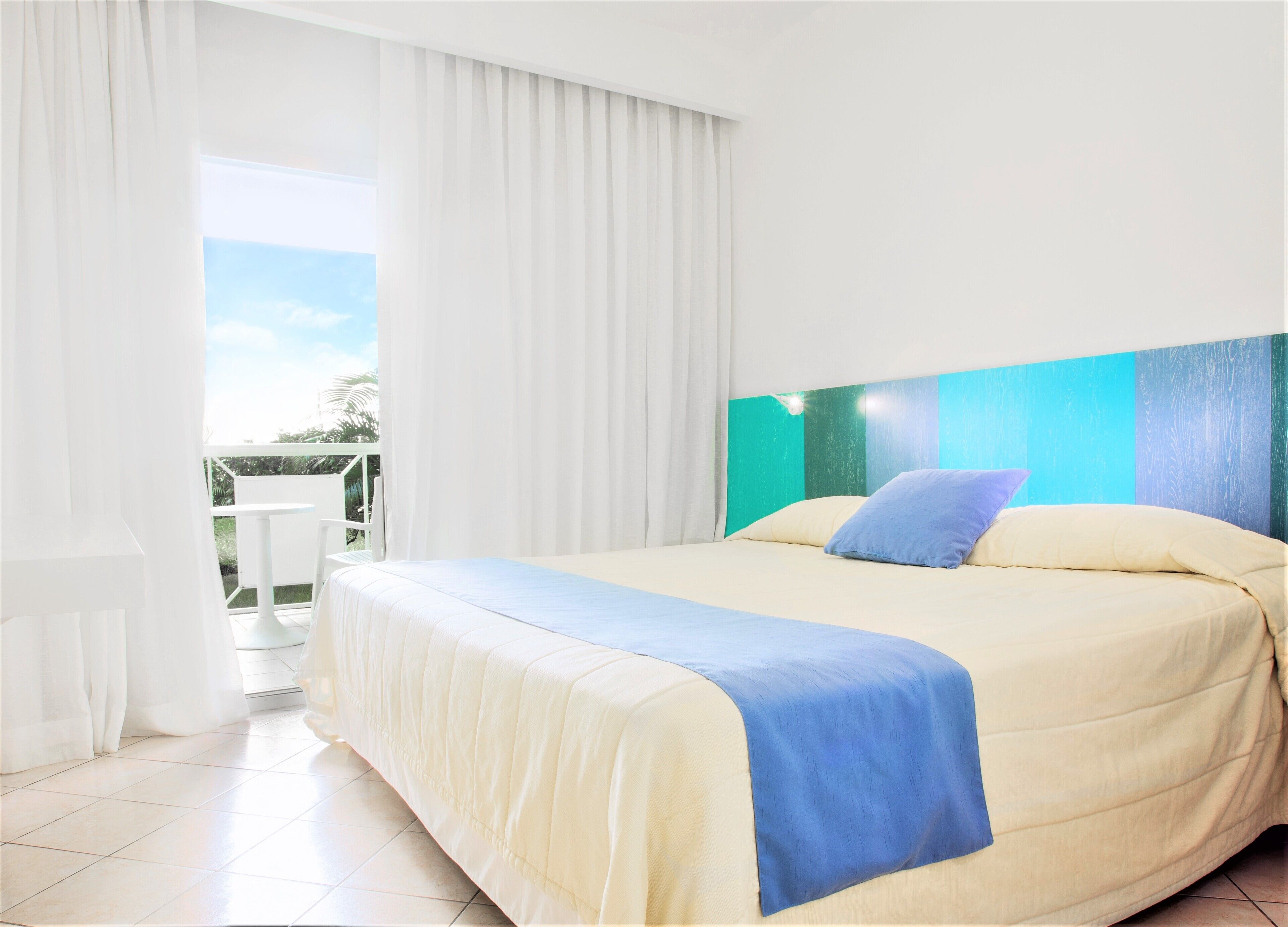 Een hotelkamer met een bed, een balkon met een tafel en gordijnen.