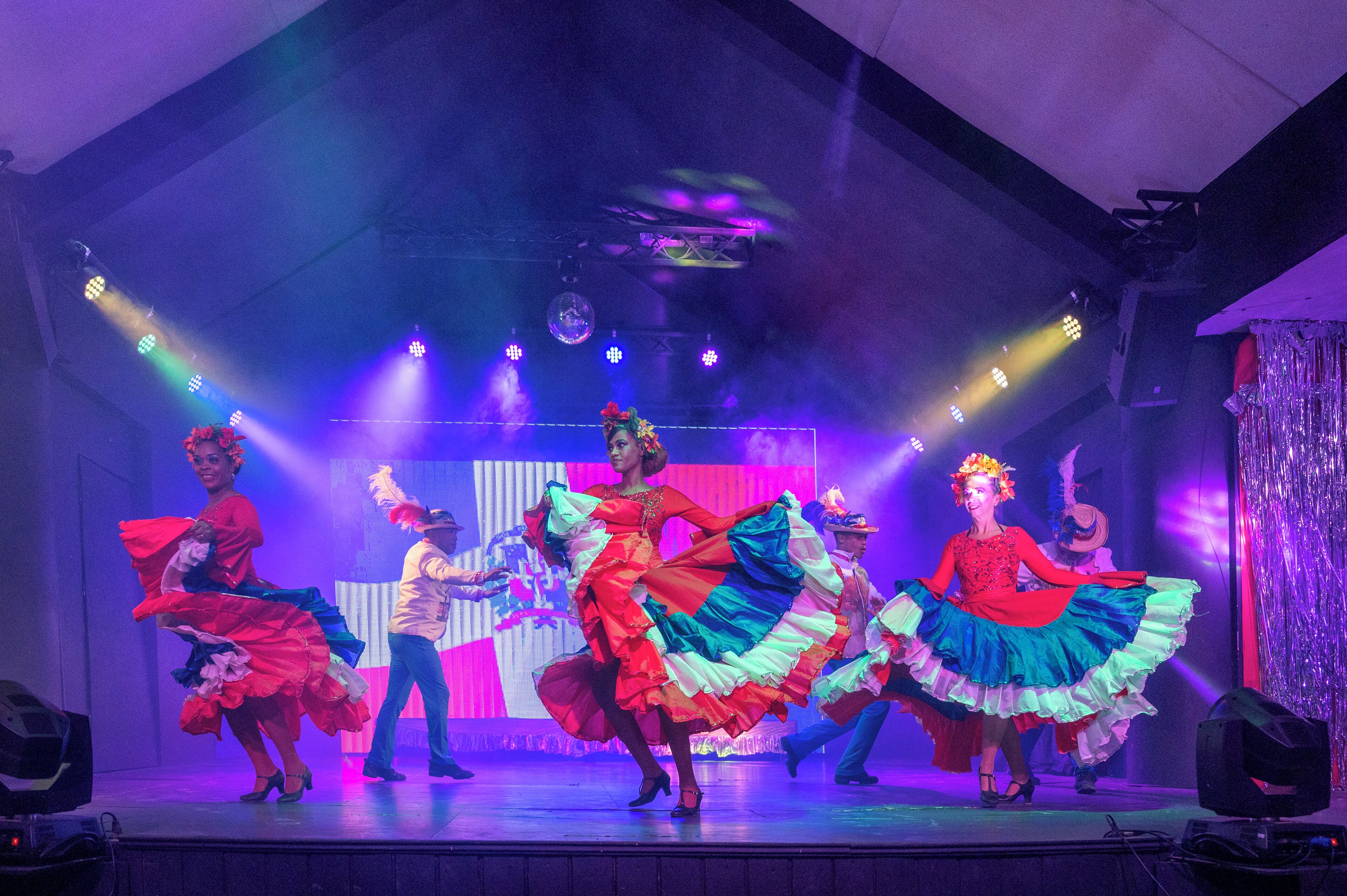 A stage with performers in colorful traditional dresses, a disco ball, and stage lighting.