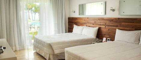 A hotel room with two beds, a wooden headboard, a desk with a chair, and a view of a pool through the window.
