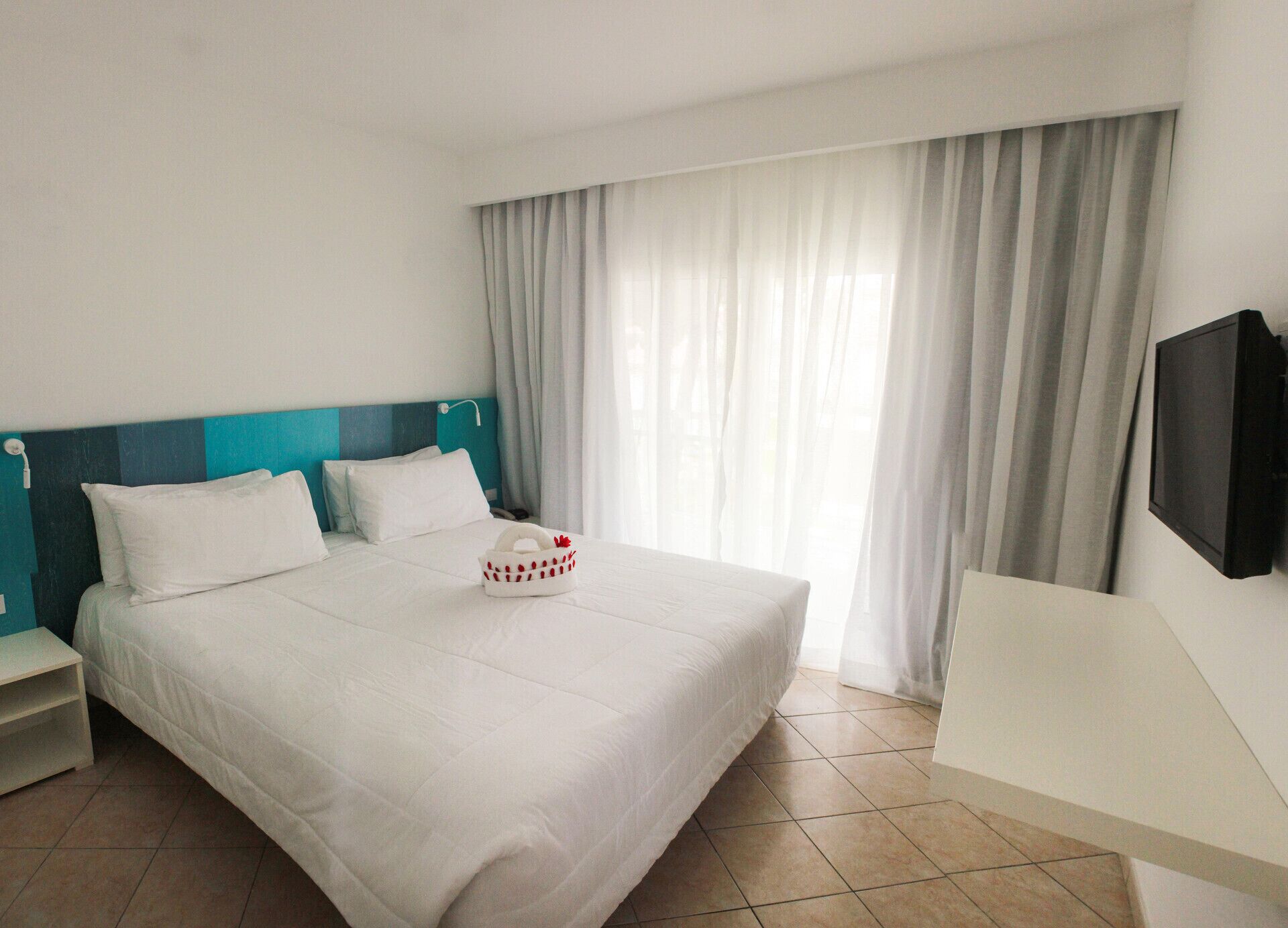 Ein Hotelzimmer mit Bett, Nachttisch, Fernseher und einem Fenster mit Vorhängen.