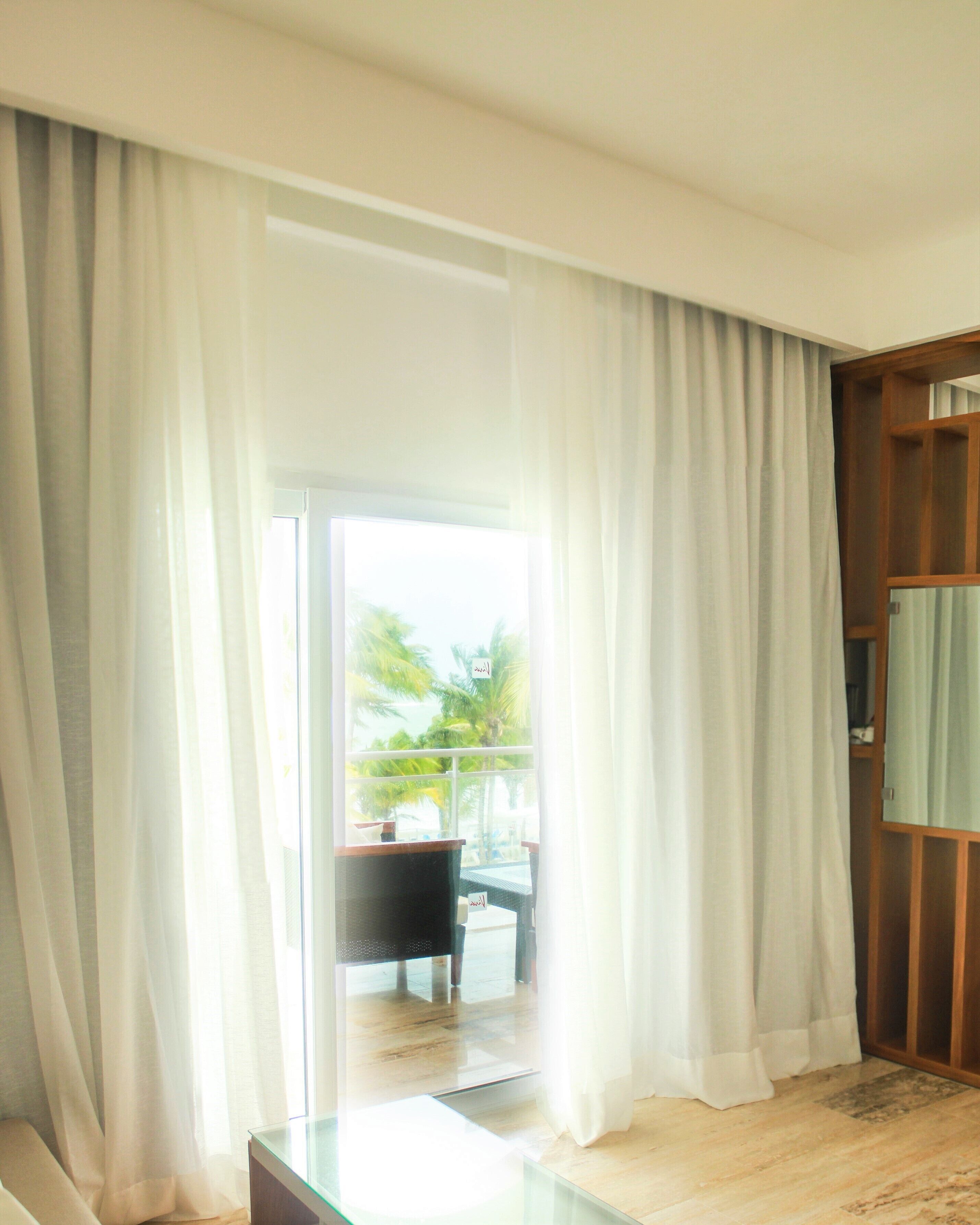 Una habitación con puerta de cristal que da a un balcón con vistas a palmeras.