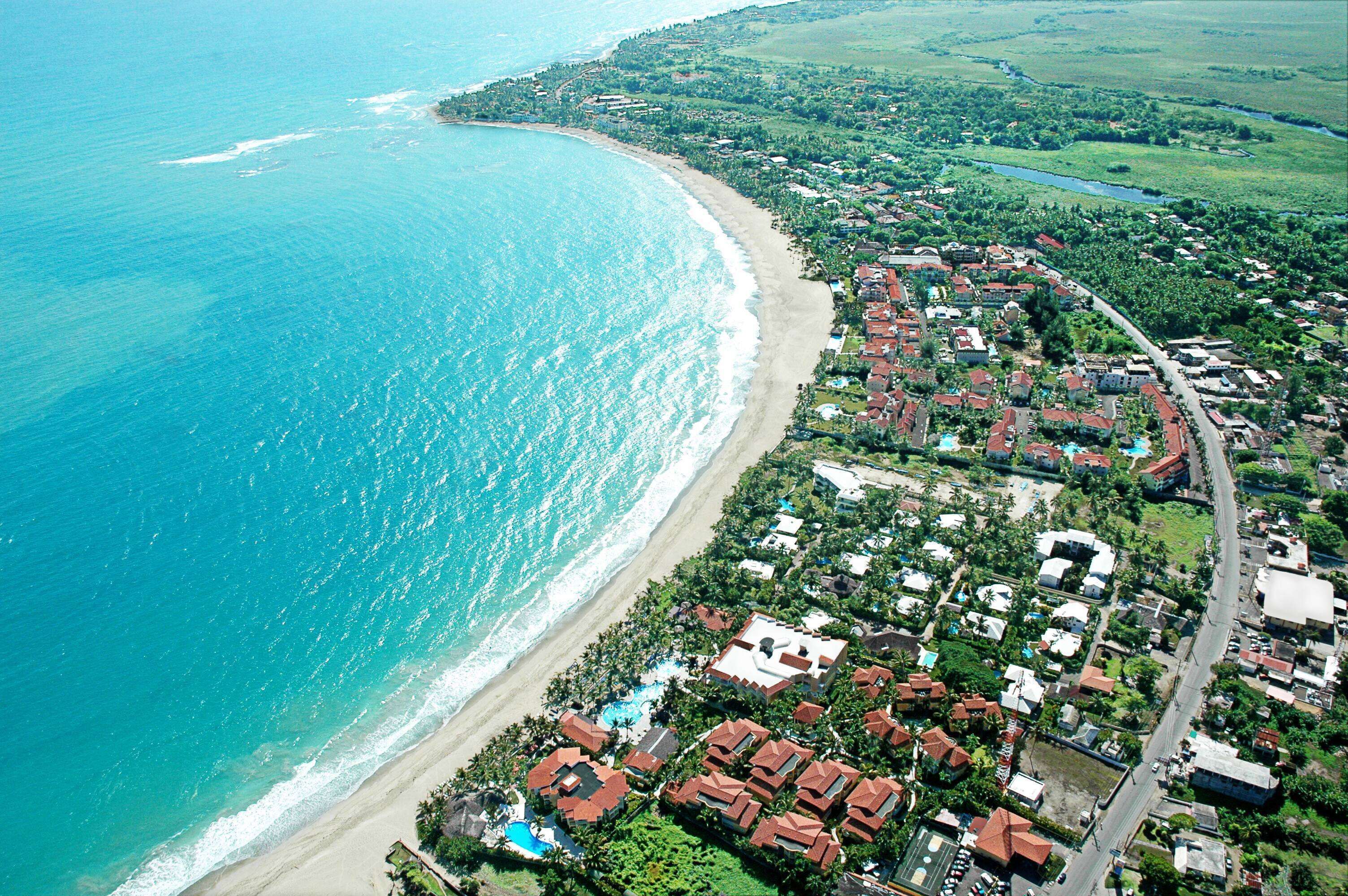 An aerial view of a coastal town with a beach, residential buildings, and a road.
