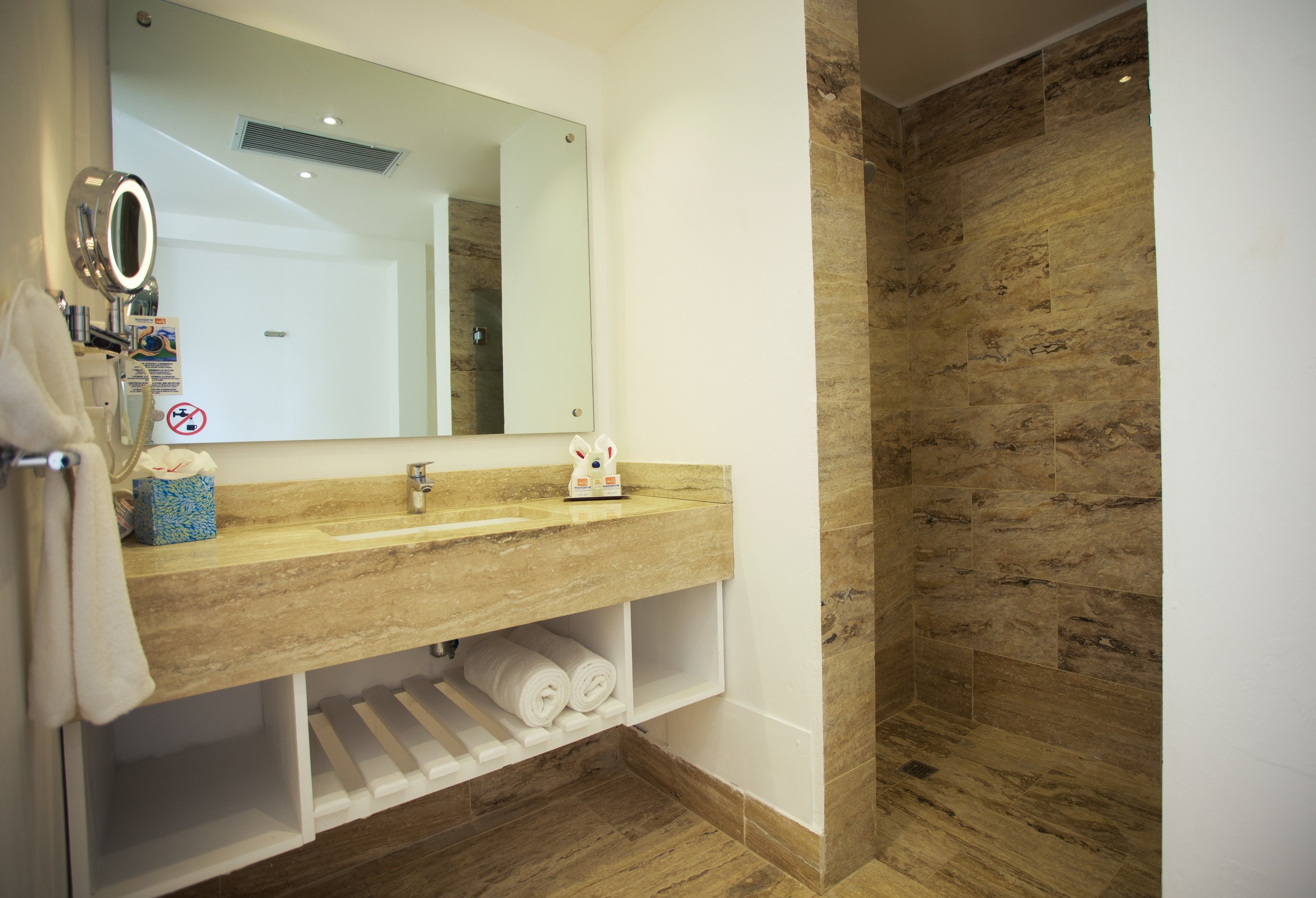 Un baño moderno con tocador de madera, un espejo grande y una zona de ducha con baldosas de piedra.