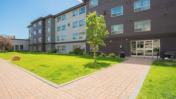 A multi-story hotel with a paved courtyard, a small tree, and a well-maintained lawn.