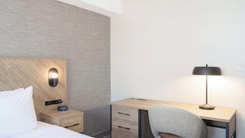 Habitación de hotel con cama, escritorio, silla, lámpara y mesita de noche con radio.