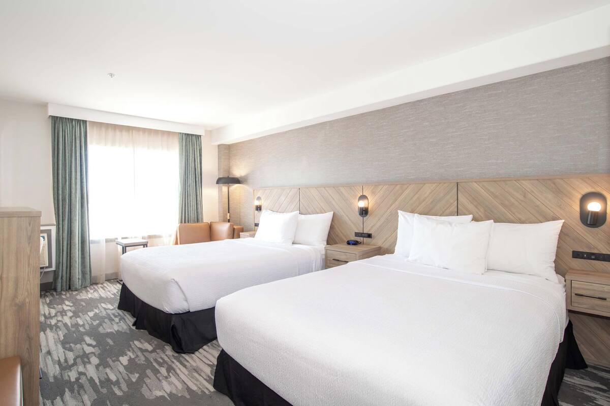 A hotel room with two beds, a desk, a chair, and a large window with curtains.