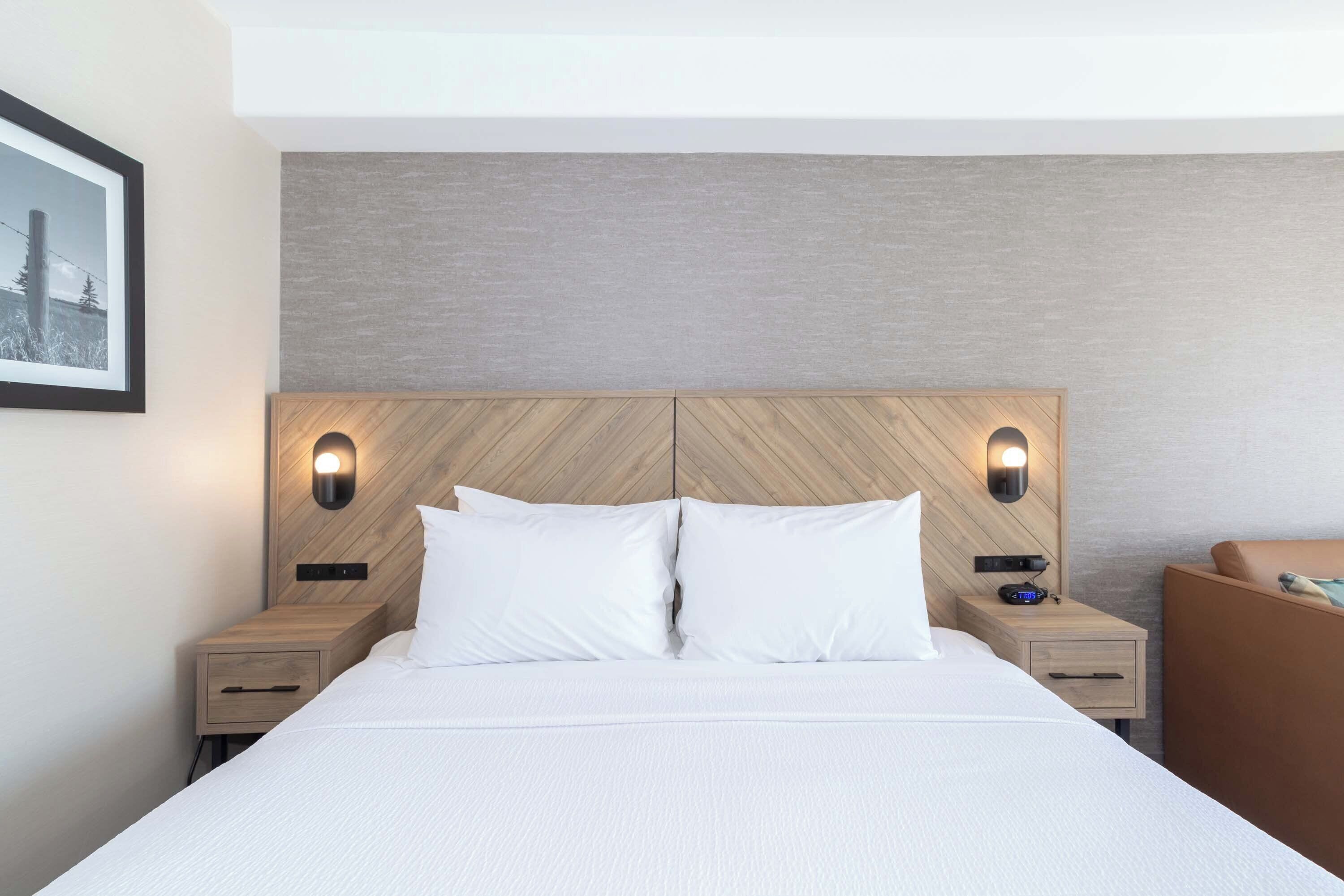 Una habitación de hotel con una cama grande, dos mesitas de noche y un cabecero con iluminación integrada.