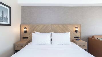 Una habitación de hotel con una cama grande, dos mesitas de noche y un cabecero con iluminación integrada.