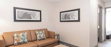 A modern living room with a beige sofa, two patterned cushions, a wooden coffee table, and two framed black-and-white photographs on the walls.