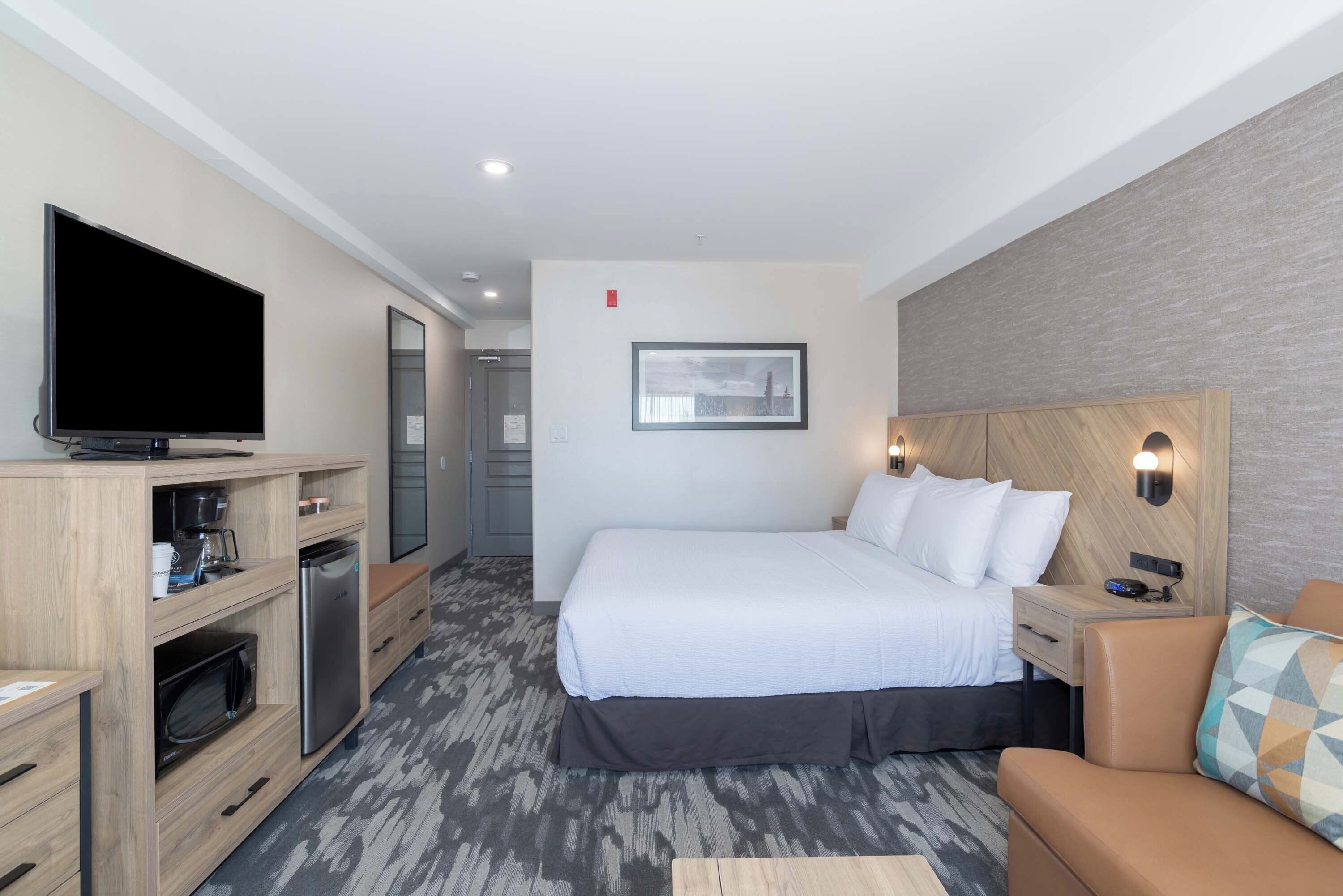 A modern hotel room with a large bed, a flat-screen TV, a microwave, a coffee maker, a desk, and a sofa.