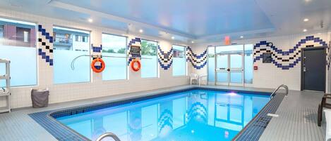 An indoor swimming pool with clear blue water, tiled walls, and a ceiling with recessed lighting.