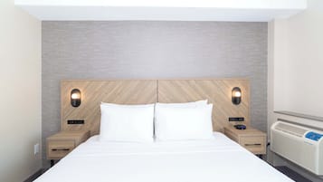A modern hotel room with a large bed, two bedside tables, a built-in heater, and wall-mounted lighting.