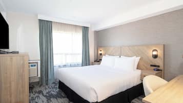 A hotel room with a large bed, a desk, a chair, a wardrobe, and a window with curtains.