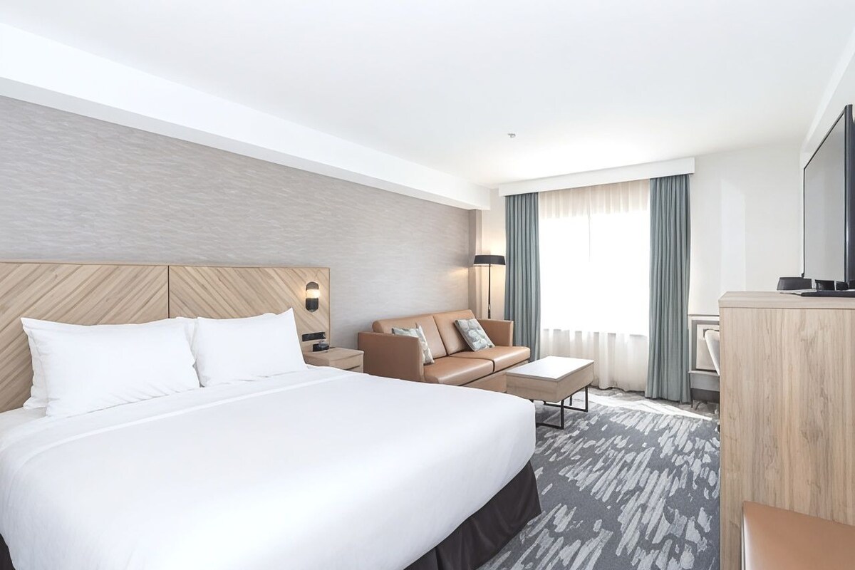 A hotel room with a large bed, a sofa, a desk, and a television.