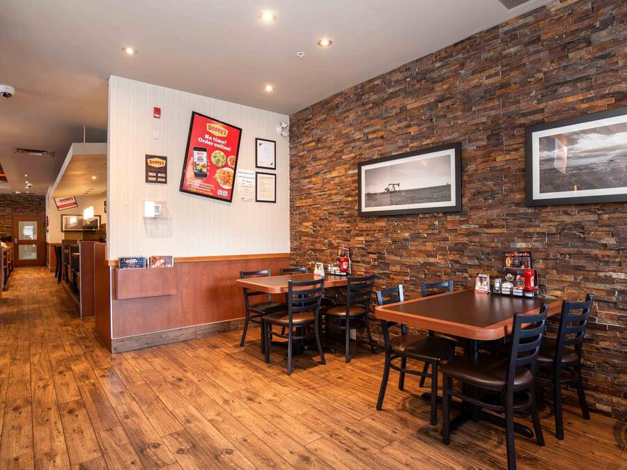 Interior de restaurante com piso de madeira, decoração de parede de pedra e várias mesas e cadeiras.