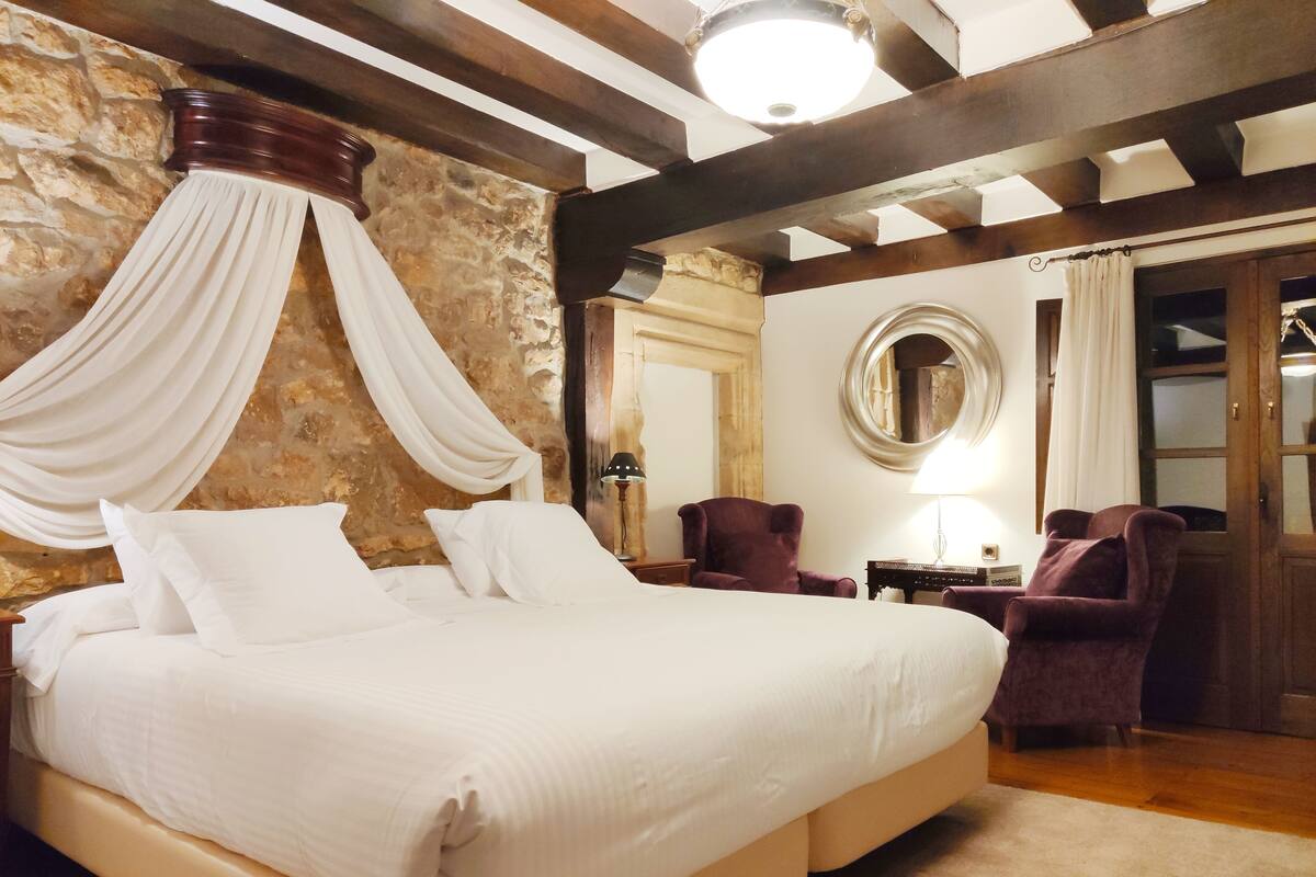 Une chambre avec un grand lit, un mur en pierre, un plafond en bois et un miroir.