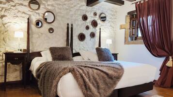Un dormitorio con pared de piedra, una cama con manta marrón, dos mesitas de noche con lámparas y una ventana con cortinas.