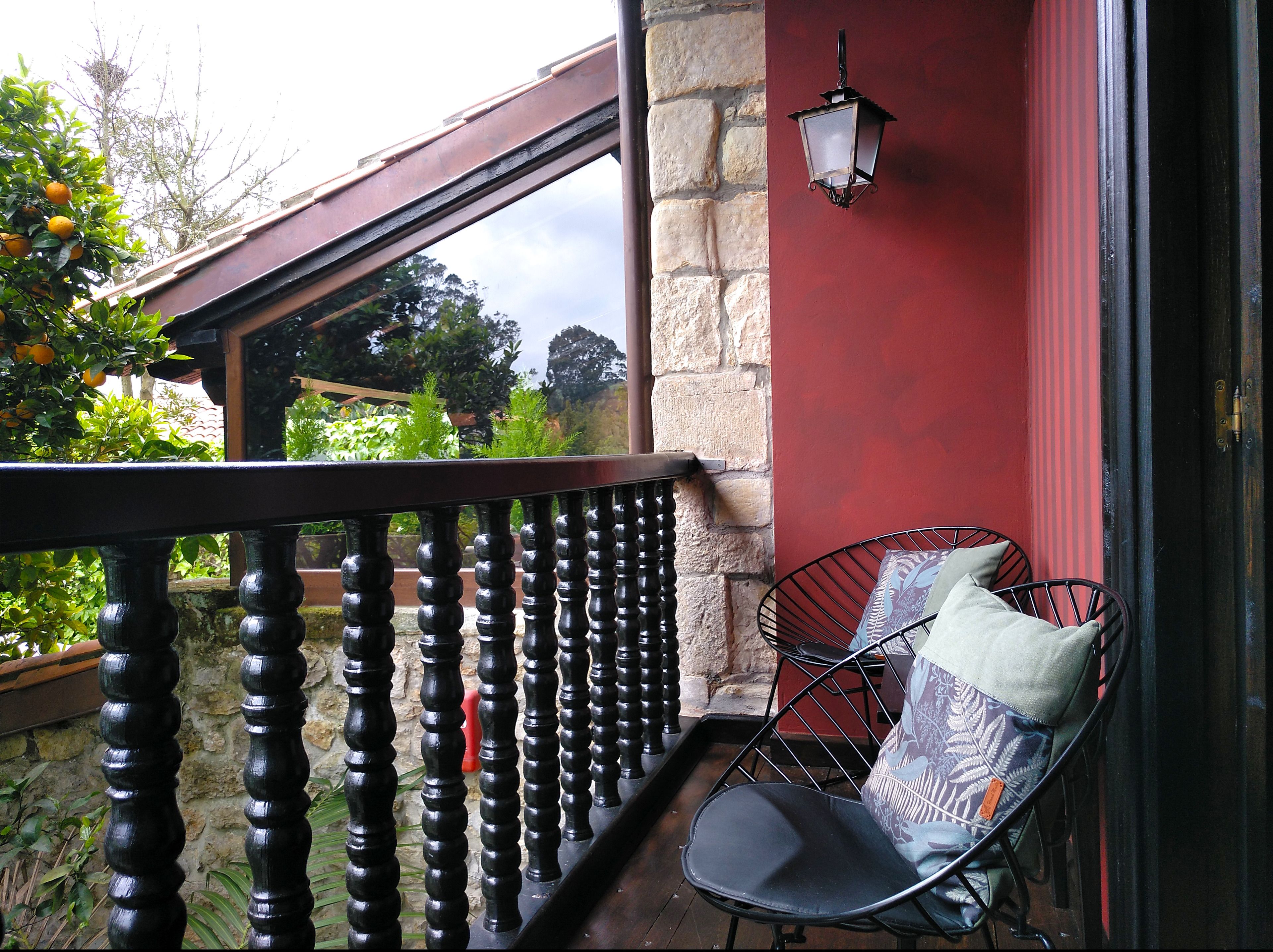 Een balkon met een smeedijzeren hekwerk, een enkele stoel met een kussen, en een lantarn aan de muur bevestigd.
