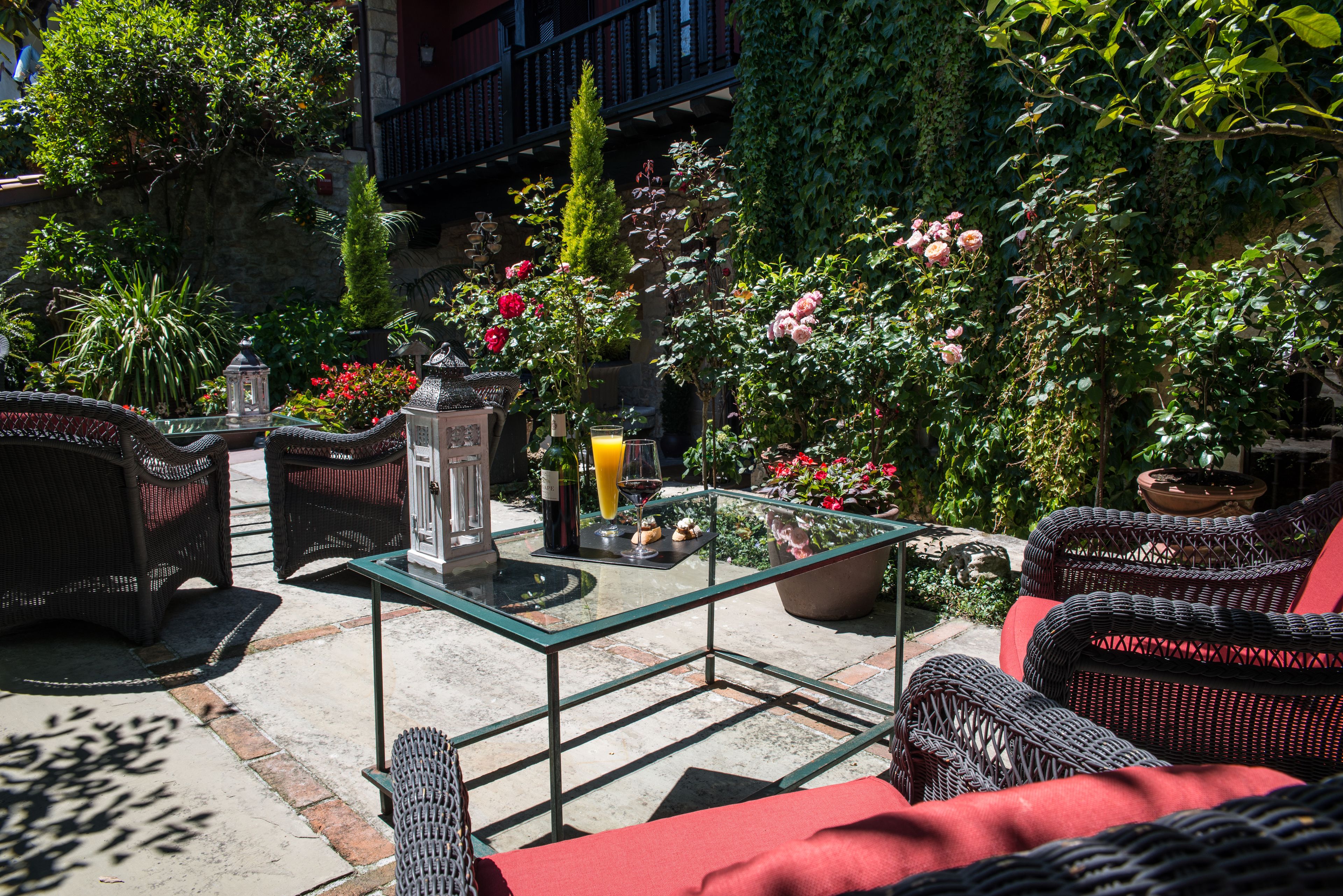 Un patio al aire libre con mobiliario de mimbre, una mesa de vidrio y plantas en macetas.
