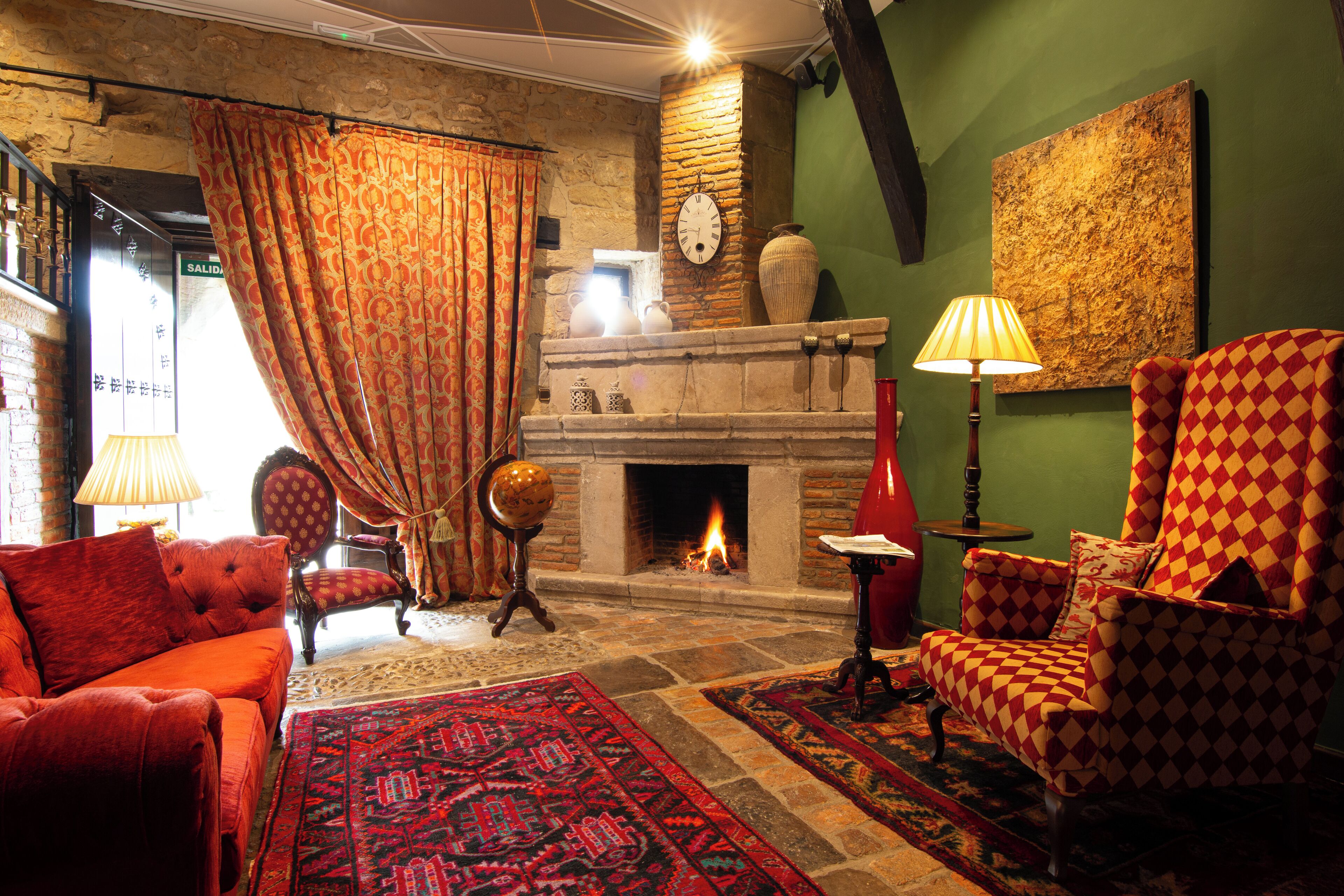 A cozy living room with a fireplace, red and orange armchairs, a patterned rug, and a globe on a stand.