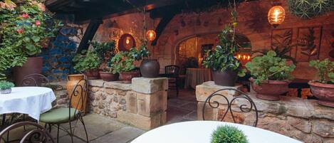 Un patio al aire libre con paredes de piedra, plantas en macetas y muebles rústicos.