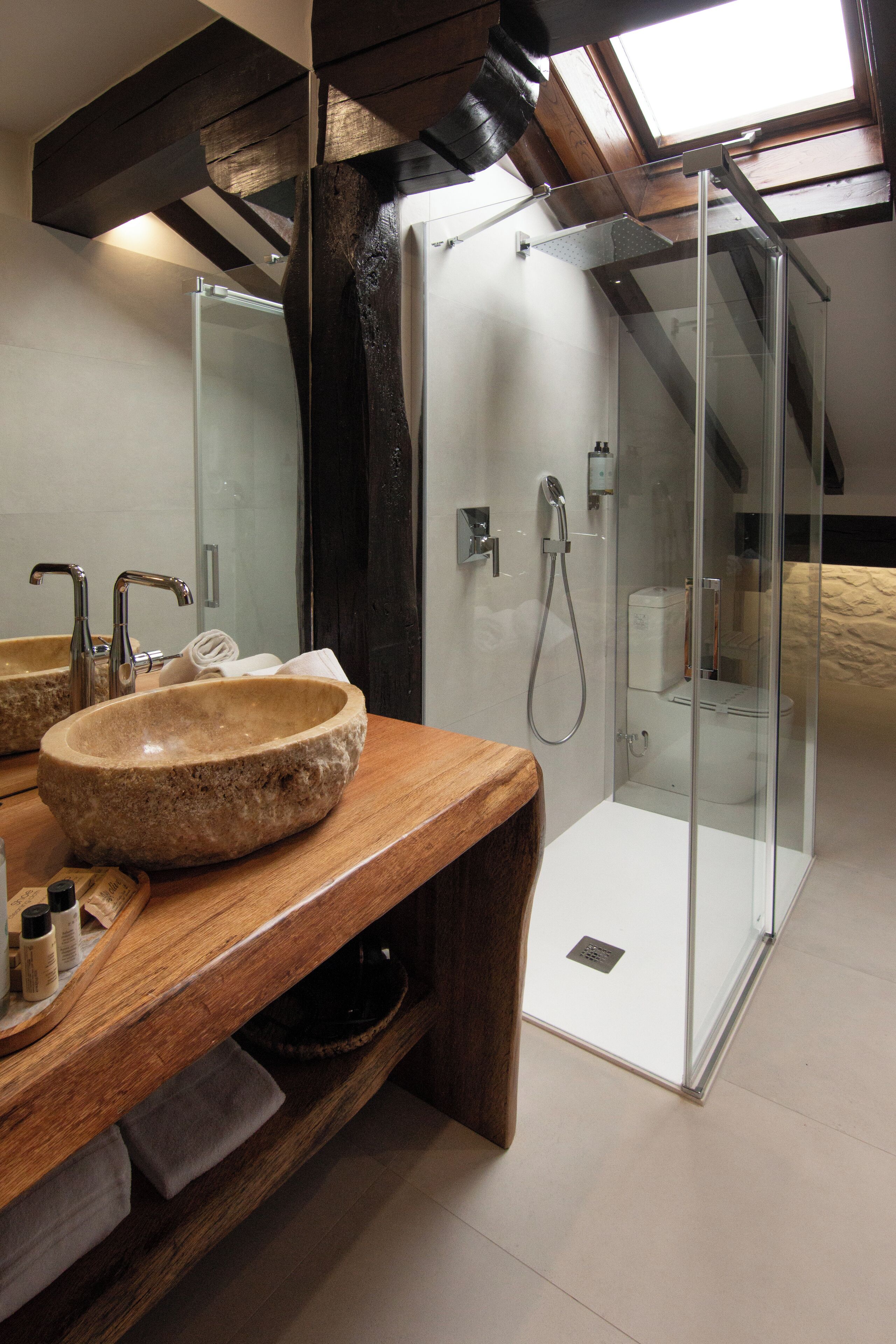 Un baño con lavamanos de piedra, tocador de madera y ducha con mampara de vidrio.