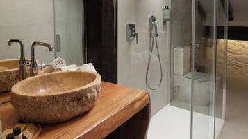 Un baño con lavamanos de piedra, tocador de madera y ducha con mampara de vidrio.