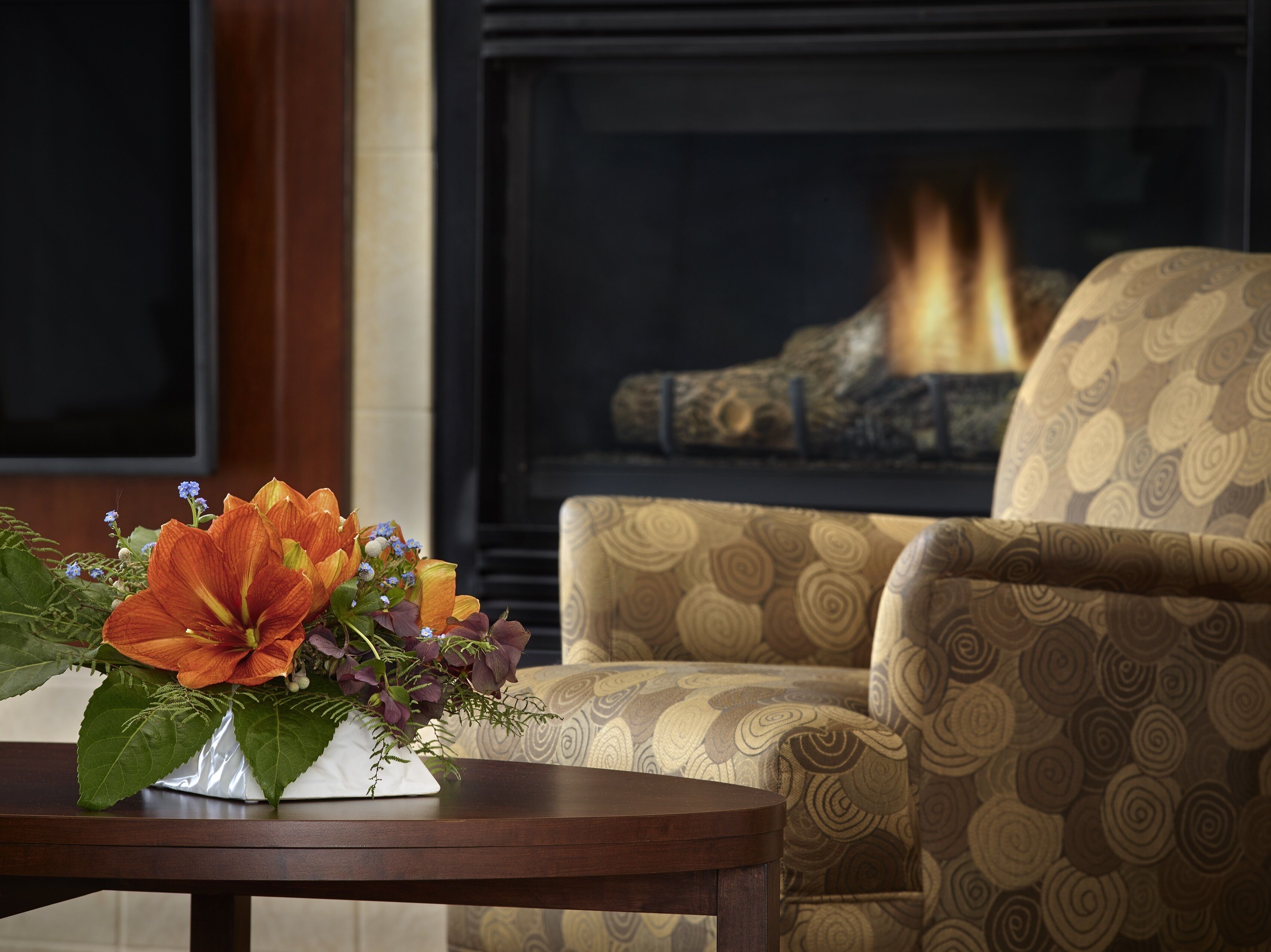 Una sala de estar con chimenea, un sillón estampado y una mesa con un arreglo floral.