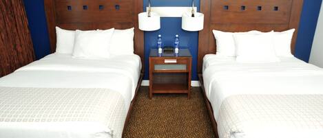 Habitación de hotel con dos camas, una mesita de noche con dos lámparas y una pequeña mesa con dos botellas de agua.