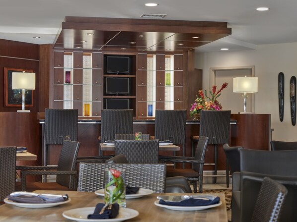 Un comedor de hotel con sillas de mimbre, un televisor central y un centro de mesa floral.