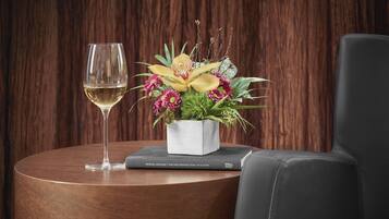 Una mesa redonda de madera con una copa de vino blanco, un libro titulado 'The Five Dysfunctions of a Team' de Patrick Lencioni, y un arreglo floral en una maceta blanca.