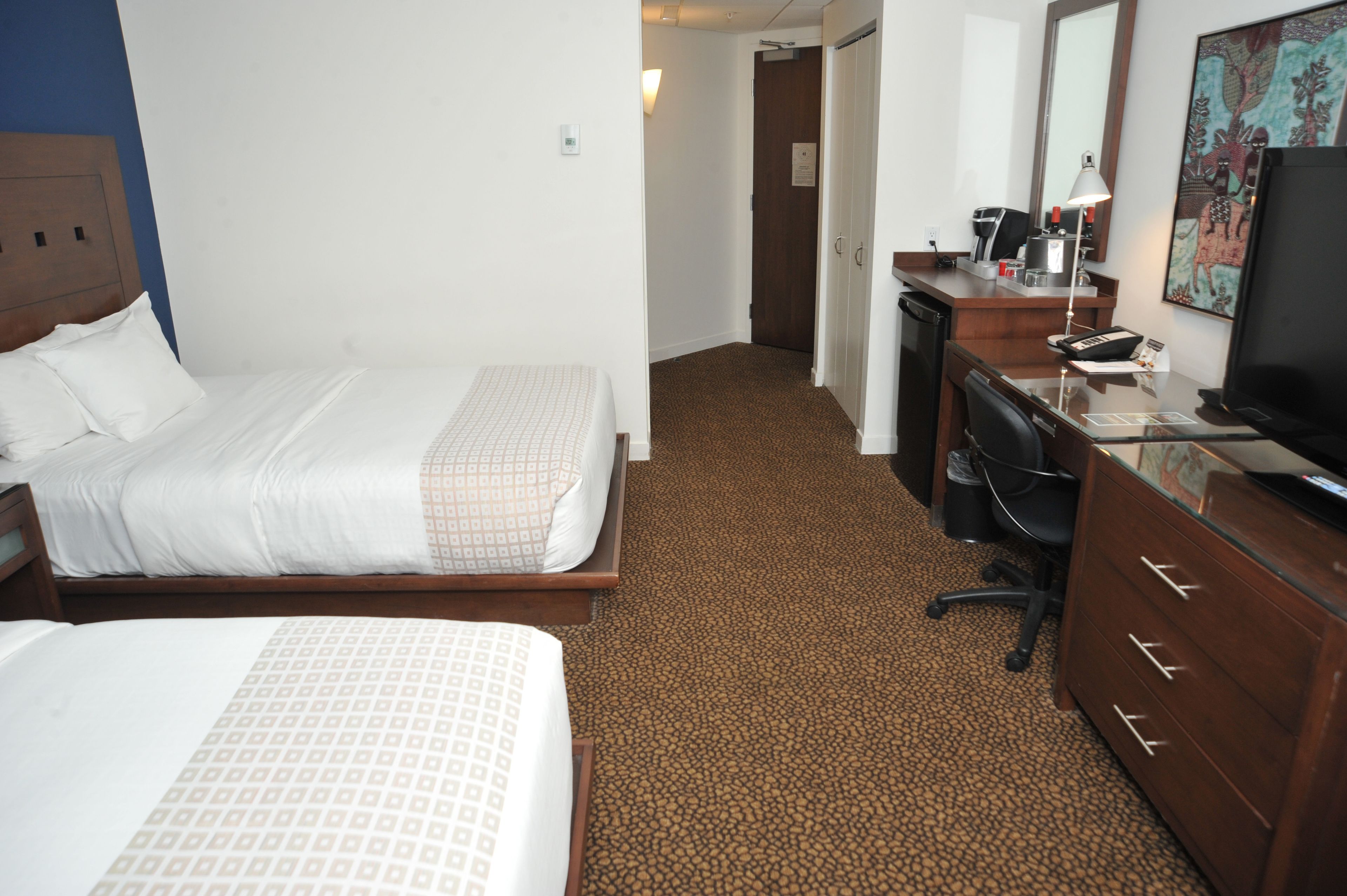 A hotel room with a bed, a desk, a chair, a dresser, a television, and a painting on the wall.