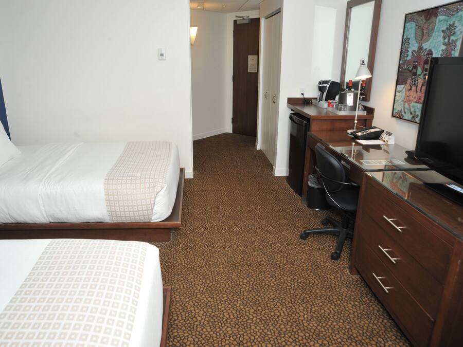 A hotel room with a bed, a desk, a chair, a dresser, a television, and a painting on the wall.