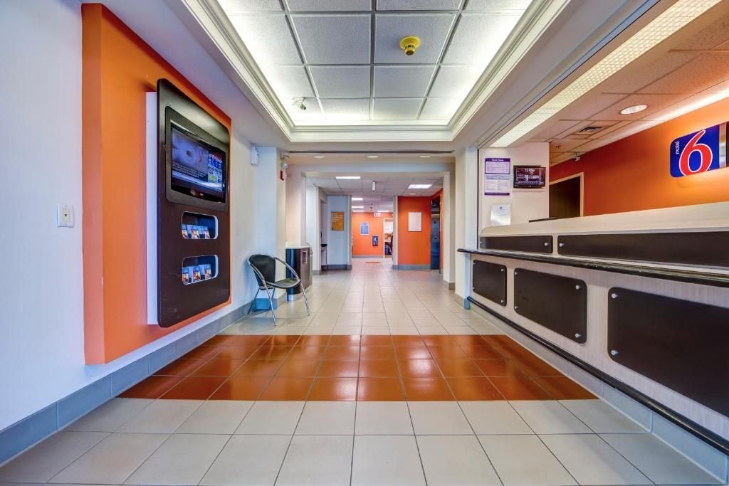 Un hall d’hôtel comprenant un comptoir d’accueil, un kiosque en libre-service et un espace détente avec des sièges.
