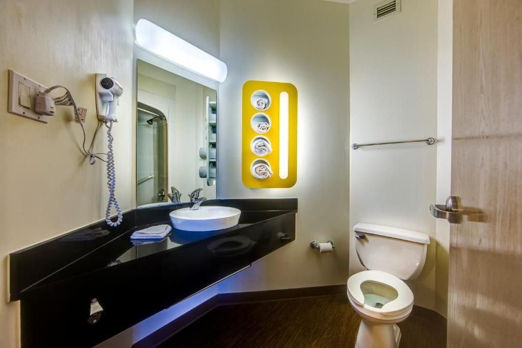 Une salle de bain avec un meuble-lavabo noir, un lavabo blanc, un sèche-cheveux et des toilettes.