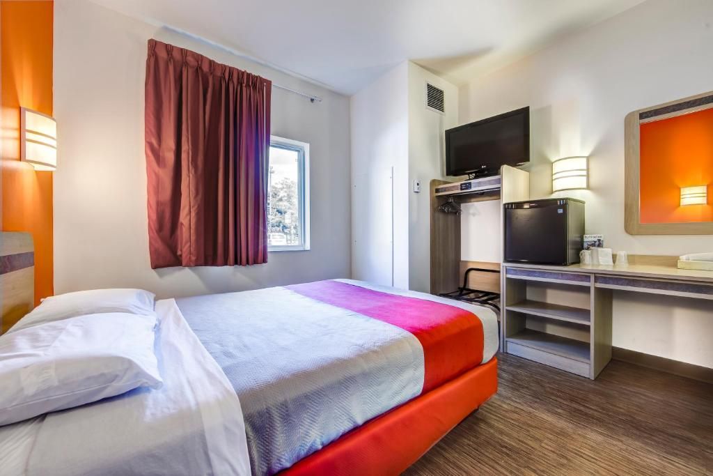 Une chambre d’hôtel équipée d’un lit, d’une télévision, d’un bureau avec un ordinateur et d’une fenêtre avec des rideaux.