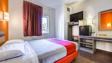 Une chambre d’hôtel équipée d’un lit, d’une télévision, d’un bureau avec un ordinateur et d’une fenêtre avec des rideaux.