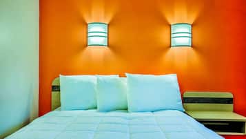 A bed with a white quilt and pillows, a wooden headboard, and two wall-mounted lights against an orange wall.