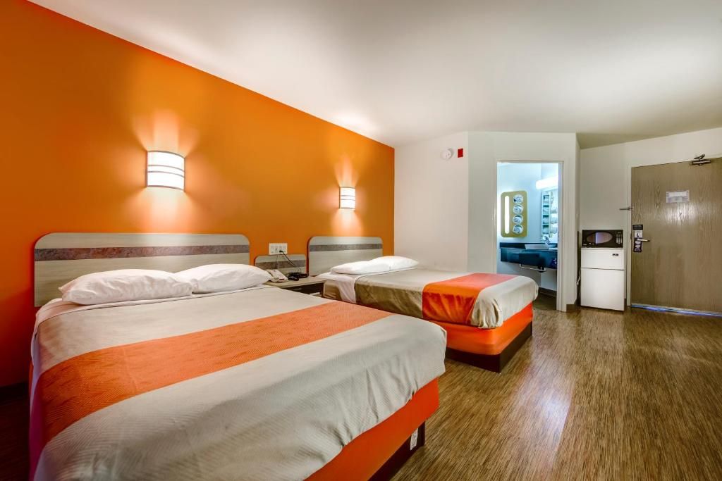 A hotel room with two beds, a kitchenette, and a bathroom visible through an open door.