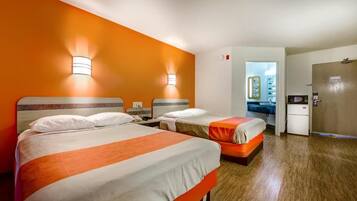 A hotel room with two beds, a kitchenette, and a bathroom visible through an open door.