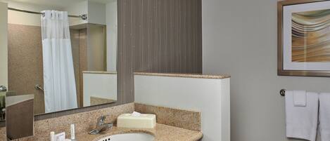 A bathroom with a granite countertop sink, a mirror, a shower curtain, and a framed picture on the wall.