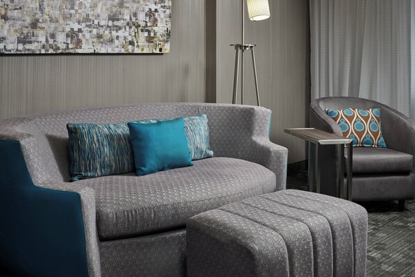 A modern hotel room with a grey sofa, matching ottoman, and a small side table. - Courtyard by Marriott Bristol (Bristol)