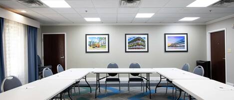 Un salón de conferencias con una larga mesa, sillas e imágenes enmarcadas en la pared.