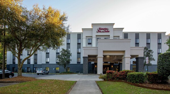 A Hampton Inn & Suites building with a modern facade, a covered entrance, and a parking area.