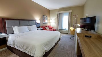 A hotel room with a large bed, a desk with a TV, a chair, and a window with curtains.