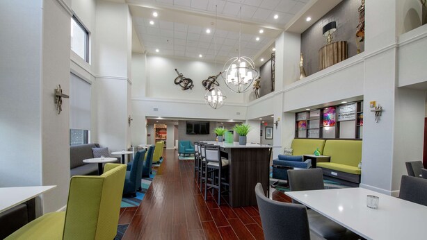A modern hotel lobby with a central bar area, seating arrangements, and a high ceiling with decorative lighting. - Hampton Inn & Suites Lafayette (Lafayette)