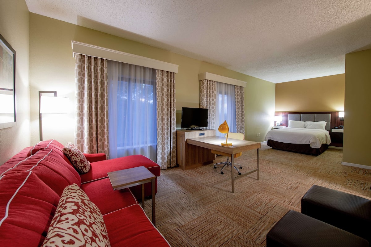 A hotel room with a red sofa, a desk with a computer, a bed, and a TV.
